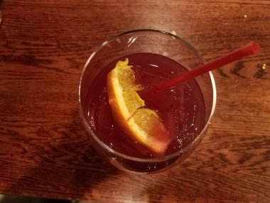 Bardakta kırmızı içecek, portakallı ve ahşap masada saman.