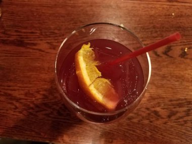 Bardakta kırmızı içecek, portakallı ve ahşap masada saman.