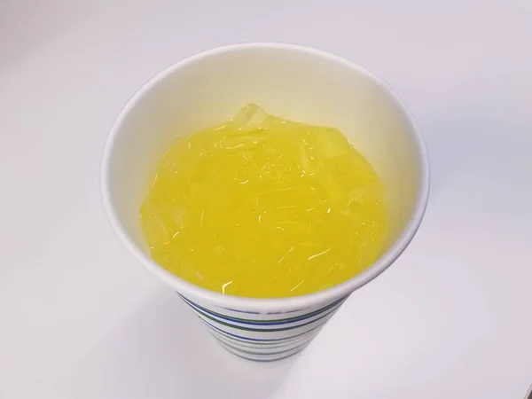 Ένα Κύπελλο Στη Λευκή Επιφάνεια Κίτρινο Υγρό Και Πάγο — Φωτογραφία Αρχείου