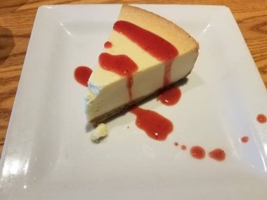 Kırmızı meyve soslu, beyaz tabakta dilimlenmiş ya da dilimlenmiş peynirli kek.
