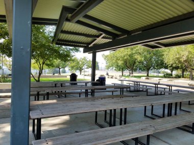 Çöp tenekesi ve bir sürü ahşap piknik masasıyla kaplı piknik alanı.