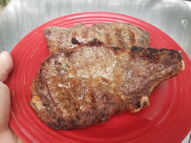 Kırmızı bir tabakta iki ızgara biftek.