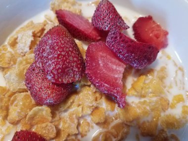 Bir kase mısır gevreği, kırmızı çilek ve süt.