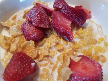 Bir kase mısır gevreği, kırmızı çilek ve süt.