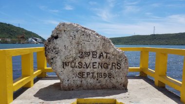 rock monument with inscription and yellow cement railing and sea water in Guanica, Puerto Rico clipart