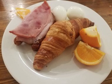Kruvasan, jambon, yumurta ve portakal dilimli tabak.