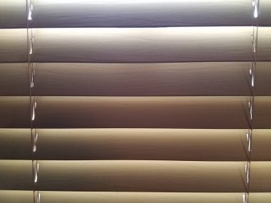 Arkalarında güneş ışığı olan kapalı kahverengi mini panjurlar.