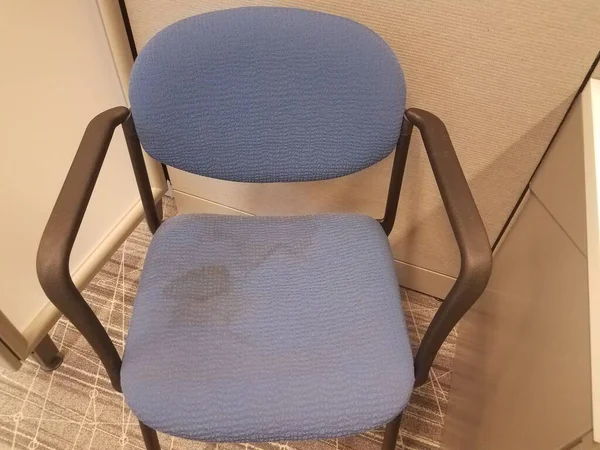 a blue office chair with stains on grey carpet in cubicle