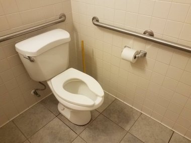 Beyaz tuvalet, fayanslar, lavabo pompası ve banyoda metal parmaklıklar olan tuvalet kağıdı.
