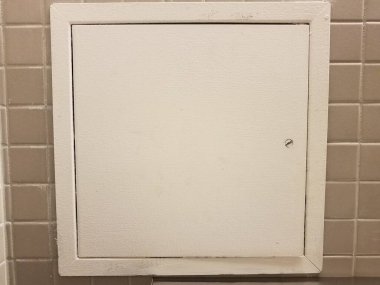 Banyodaki ya da tuvaletteki gri fayanslara beyaz kapı ya da erişim paneli