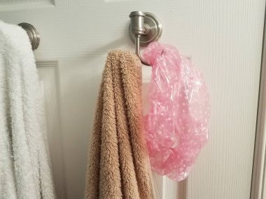 Banyonun kapısına asılı beyaz ve kahverengi havlu ve pembe duş bonesi.