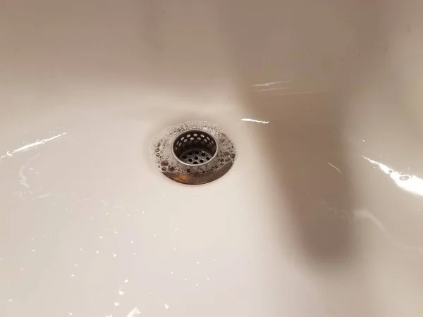 a bathroom sink with drain and water and soap bubbles