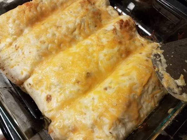 Fırında cam tavada peynirli enchiladas ve spatula.
