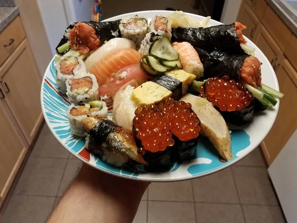 Hand holding plate of sushi raw fish and eggs in kitchen — Stock Photo, Image