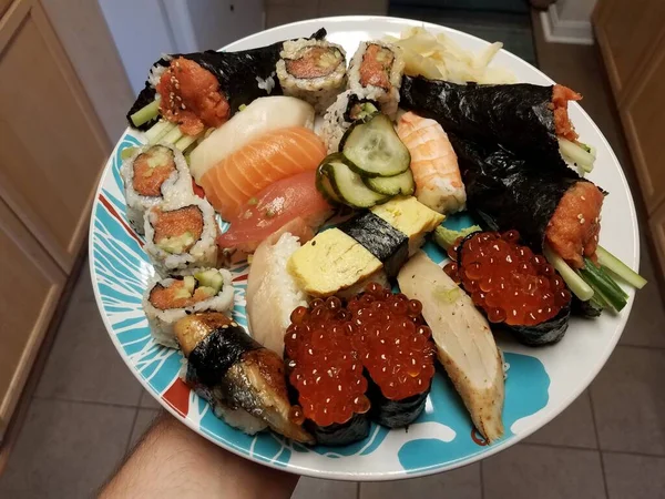 Hand holding plate of sushi raw fish and eggs in kitchen — Stock Photo, Image