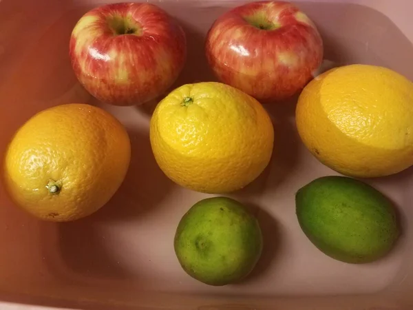 Manzanas y naranjas y limas flotando en el agua — Foto de Stock