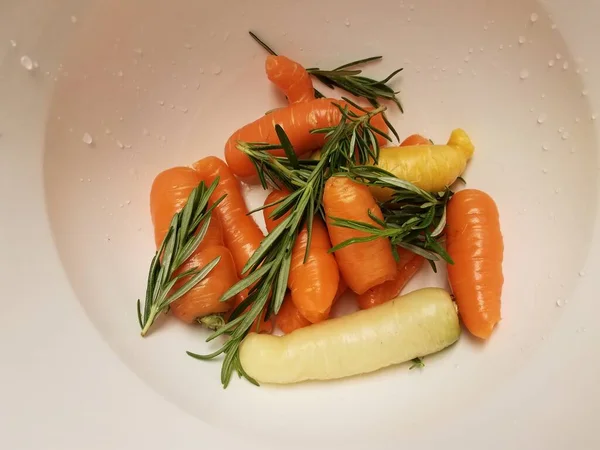 Wortelen en rozemarijn in witte recipiënt of schaal — Stockfoto