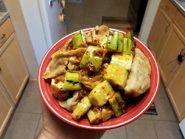 Mão segurando tigela vermelha com bolinhos chineses e pepino — Fotografia de Stock