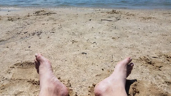 Pés masculinos na areia e seixos na praia com água — Fotografia de Stock