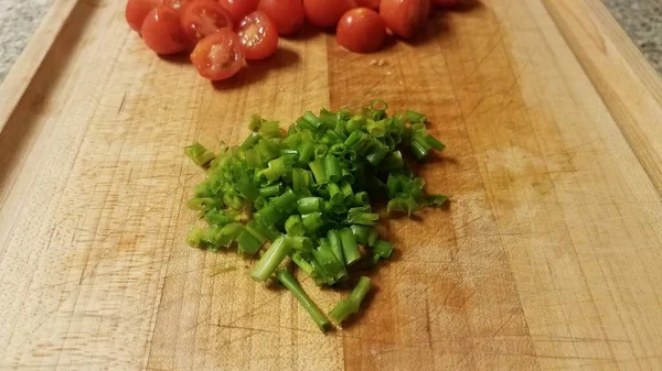 Zielone szczypiorek i czerwone pomidory na desce do krojenia — Zdjęcie stockowe