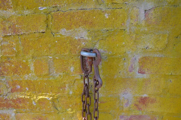 Ржавая металлическая цепь, висящая на желтом и красном кирпичах — стоковое фото
