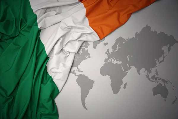 waving colorful national flag of ireland on a gray world map background.
