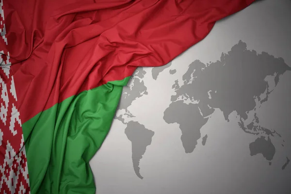 在灰色世界地图背景上挥舞着白俄罗斯多彩的国旗 — 图库照片