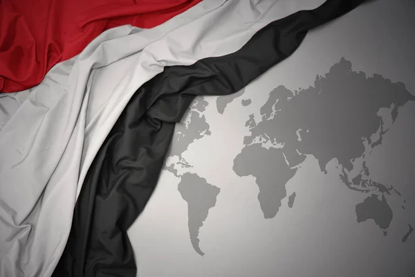 waving colorful national flag of yemen on a gray world map background.