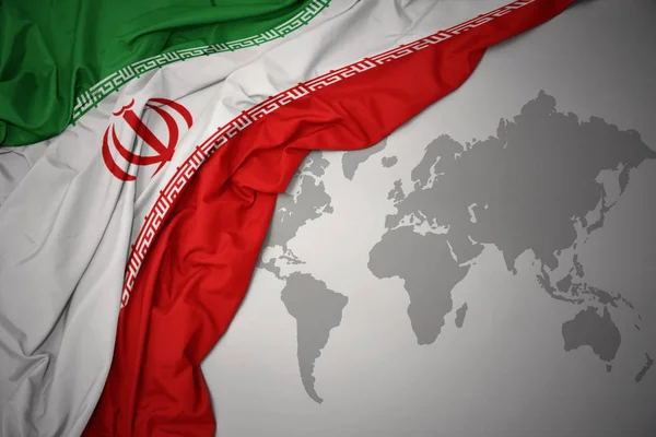 挥舞着彩色的伊朗国旗在灰色世界地图背景 — 图库照片