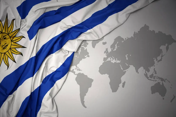 在灰色的世界地图背景上挥舞着乌拉圭多彩的国旗 — 图库照片
