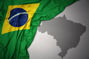 waving colorful national flag of brazil on a gray map background. clipart