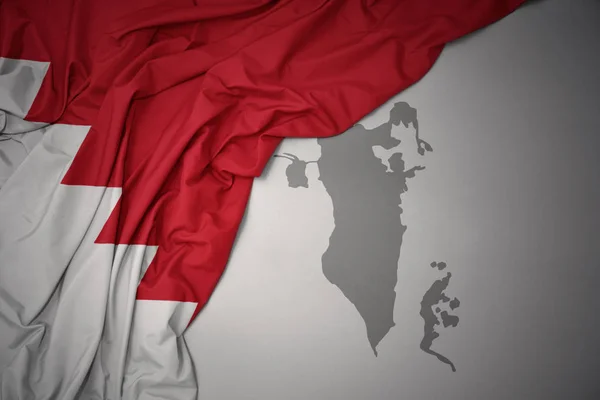 waving colorful national flag of bahrain on a gray map background.