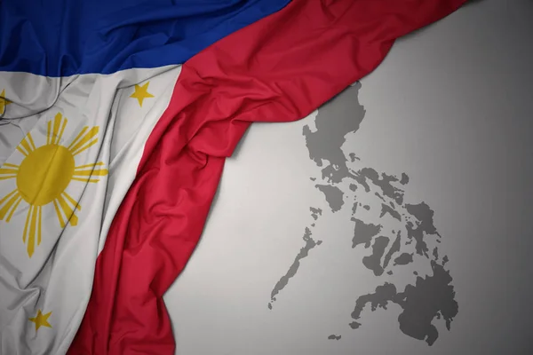 在灰色地图背景上挥舞着菲律宾多彩的国旗 — 图库照片