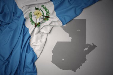 waving colorful national flag of guatemala on a gray map background. clipart