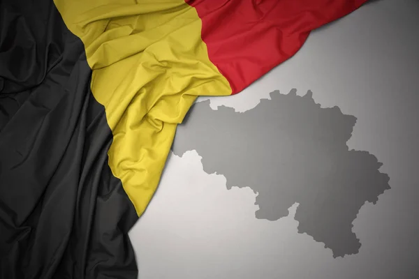 灰色のマップの背景にベルギーのカラフルな国旗を振ってください — ストック写真