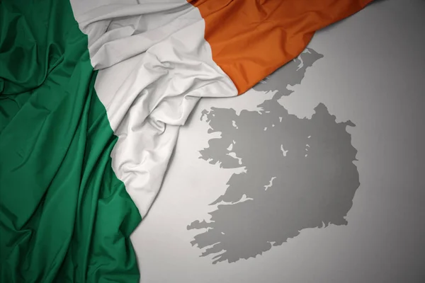 waving colorful national flag of ireland on a gray map background.