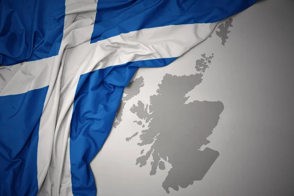 waving colorful national flag of scotland on a gray map background.