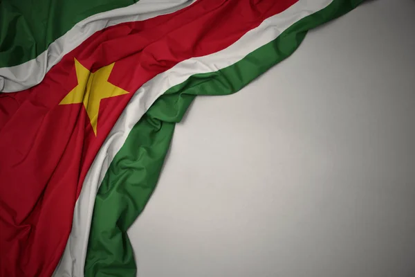 Ondeando la bandera nacional de surinam sobre un fondo gris . — Foto de Stock