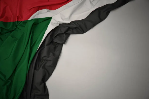 Acenando bandeira nacional de sudan em um fundo cinza . — Fotografia de Stock