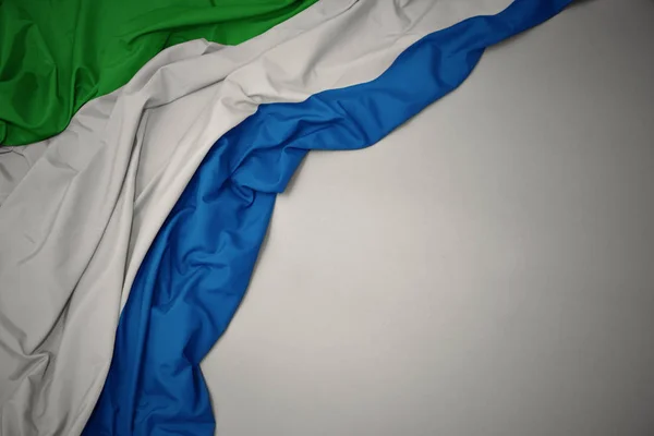 Agitant le drapeau national de la Sierra Leone sur un fond gris . — Photo