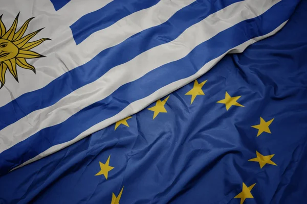 Ondeando colorida bandera de la unión europea y bandera de uruguay . —  Fotos de Stock