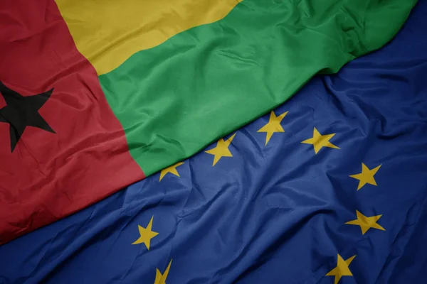 Waving colorful flag of european union and flag of guinea bissau. — Stock Photo, Image