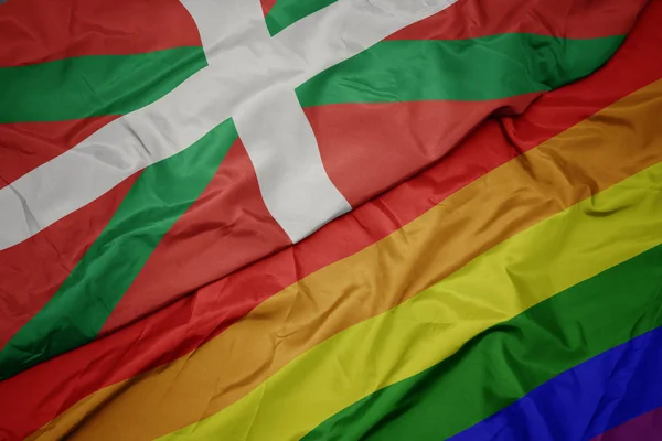 Waving colorful gay rainbow flag and national flag of basque country. — Stock Photo, Image