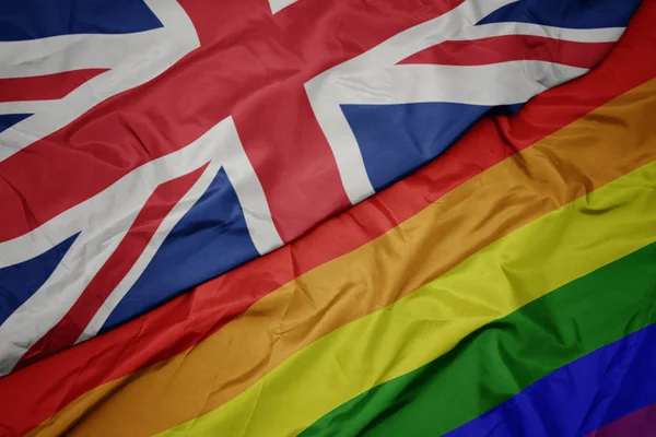 Waving colorful gay rainbow flag and national flag of great britain. — Stock Photo, Image