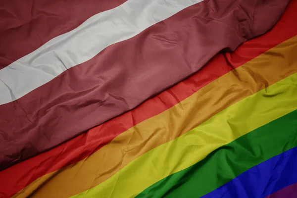 Waving colorful gay rainbow flag and national flag of latvia. — Stock Photo, Image