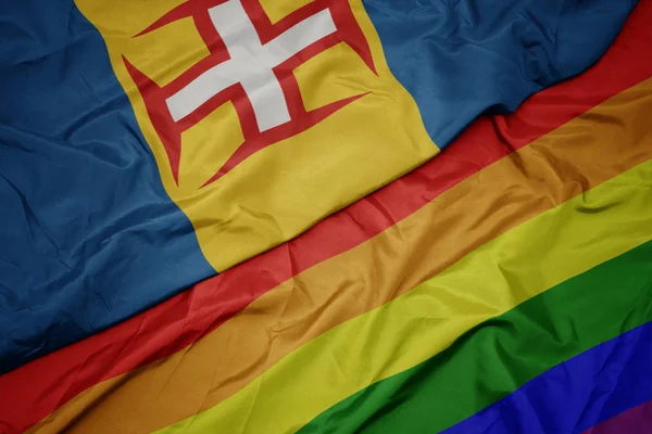 Waving colorful gay rainbow flag and national flag of madeira. — Stock Photo, Image