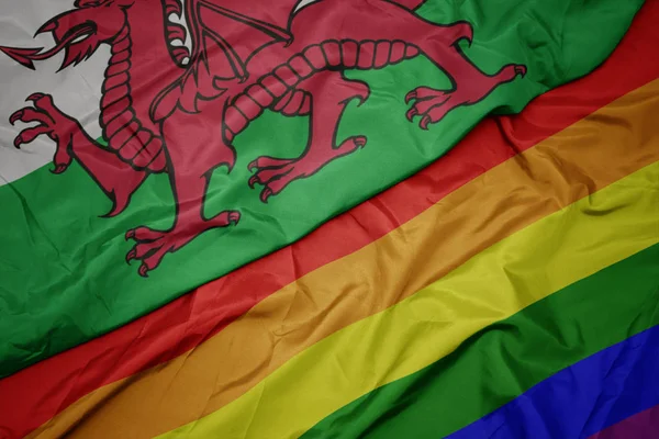 Waving colorful gay rainbow flag and national flag of wales. — Stock Photo, Image
