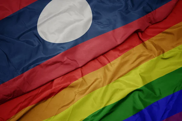 Waving colorful gay rainbow flag and national flag of laos. — Stock Photo, Image