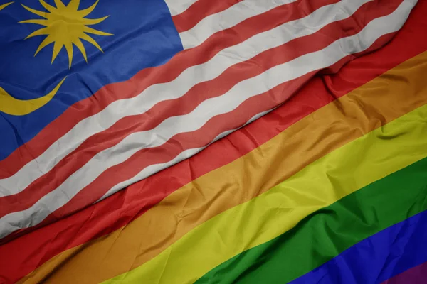 waving colorful gay rainbow flag and national flag of malaysia.