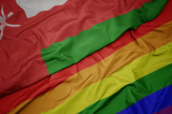 Waving colorful gay rainbow flag and national flag of oman. — Stock Photo, Image